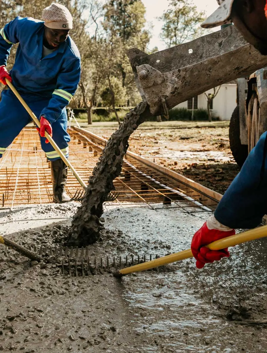 Construction workers screeding freshly poured concrete over steel reinforcing mesh on a South African site.