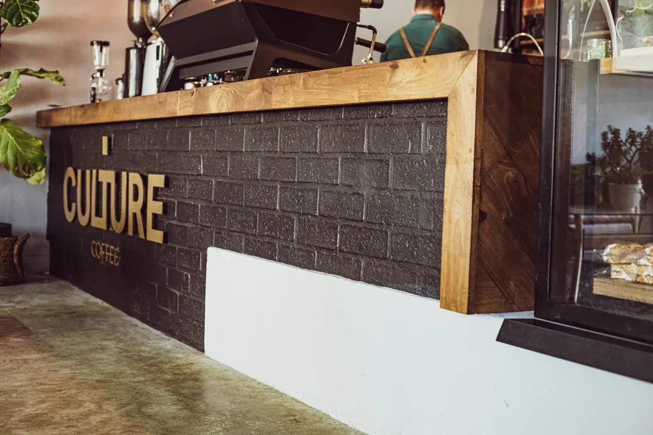 Culture Coffee: the service counter in dark painted brick with gold lettering and a solid timber top, roastery behind.