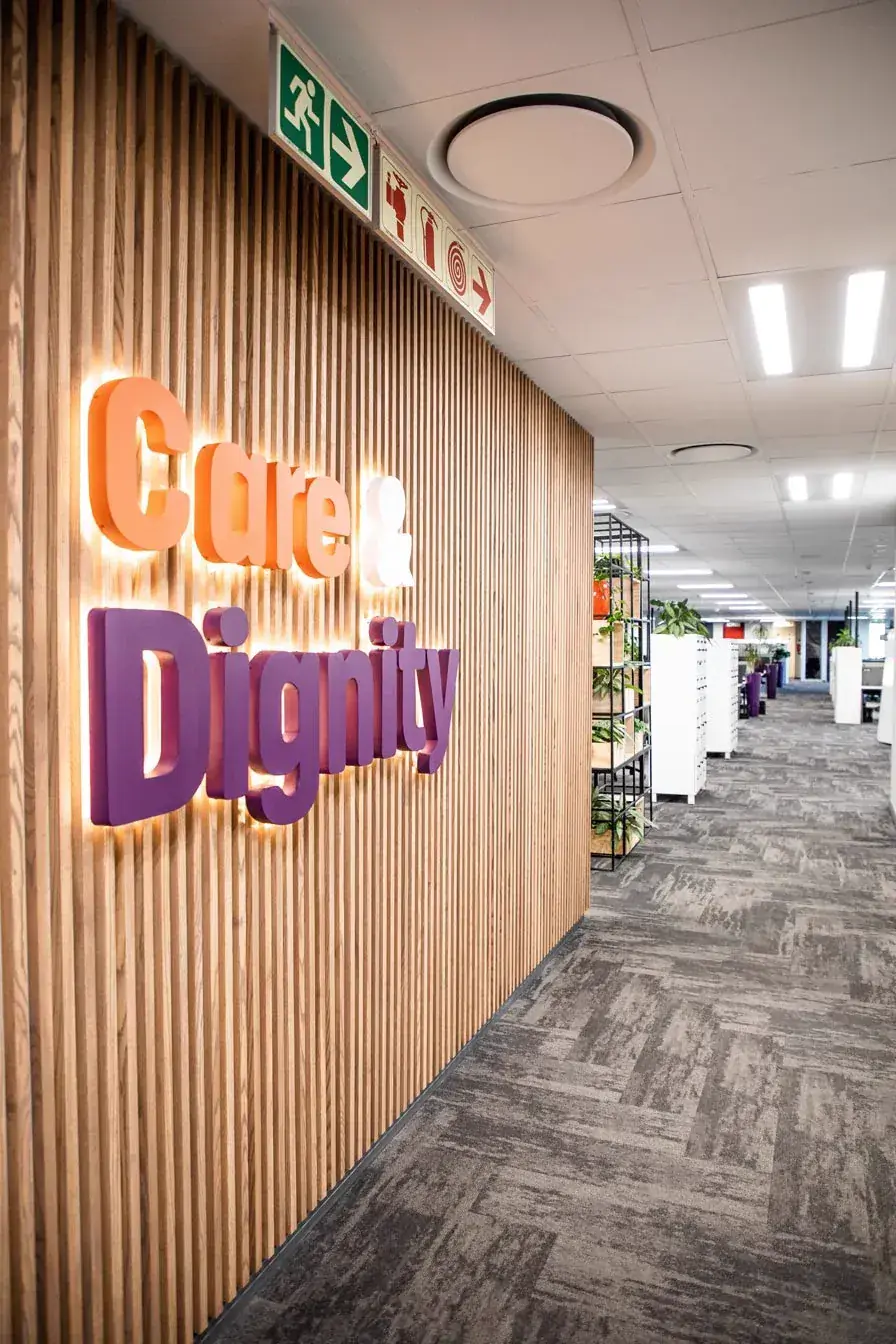 Hollard Part 2: the timber batten feature wall with illuminated Care and Dignity lettering, open plan office behind.