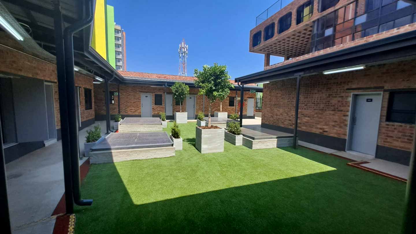 NXT Gen Phase 2: the central courtyard with artificial turf lawn, raised timber planters and brick residence wings under a clear sky.